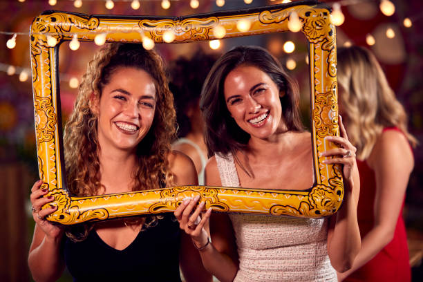 female friends having fun posing with photo booth photo frame at party in bar - feest fotos stockfoto's en -beelden