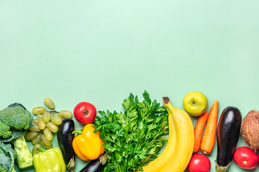 tabletop arrangement of variety of fresh fruits and vegetables sorted by colors-pepper, tomato, corn, carrot, green salad, cilantro, eggplant, cucumber, basil, dill, onion Healthy food concept.