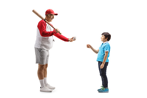 Full length profile shot of a mature man with a baseball bat giving a ball to a boy isolated on white background
