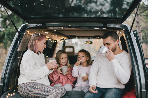Padres felices y sus hijos bebiendo cacao caliente sentados en una camioneta decorada con luces navideñas festivas. photo