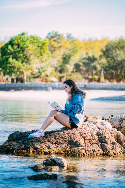 istock Beautiful Woman Reading a Book on the Beach 1352230459