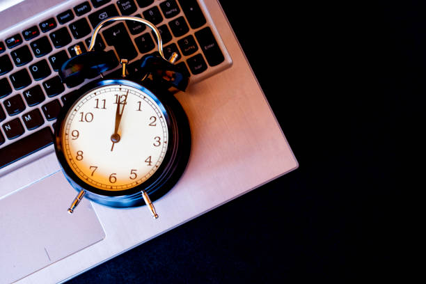istock Concept time to be in the computer. Black alarm clock on laptop. 1352231758