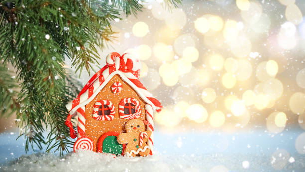 toy gingerbread house stand under fir branches in snow on background of bright bokeh lights. christmas mood. copy space. - fake snow imagens e fotografias de stock