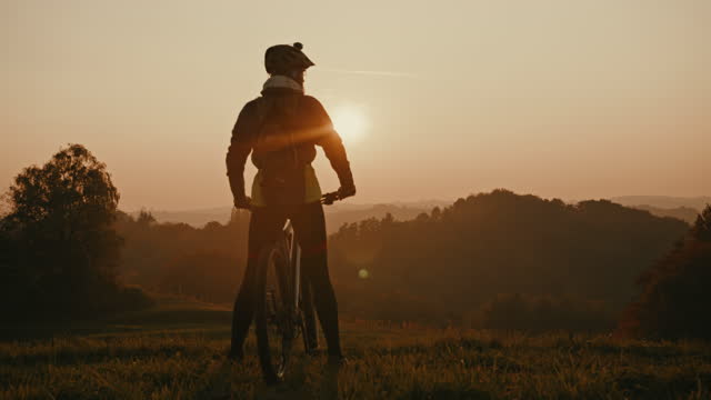 SLO MO Mountain biker enjoys the view over the countryside from the hill
