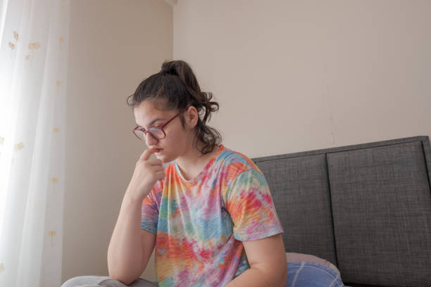 young worried school girl with eyeglasses bites her nails in her room - nail biting imagens e fotografias de stock