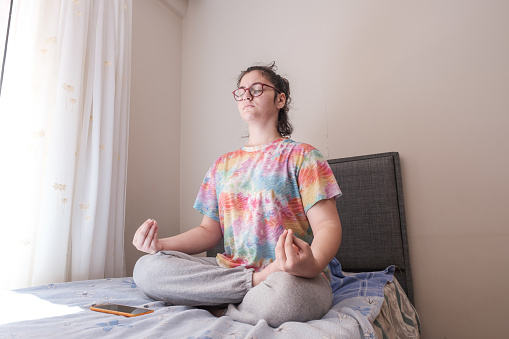 a young tween girl making Yoga gestures by closing her eyes and trying to relax in her room for relaxation resting exercising meditating concepts
