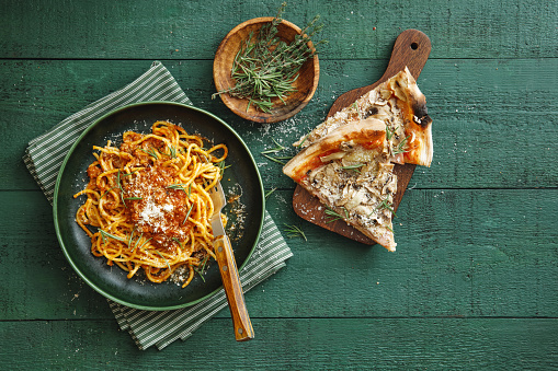 Classic spaghetti bolognese with parmesan cheese and herb. Beef-mushroom pizza. Flat lay top-down composition on dark green background.