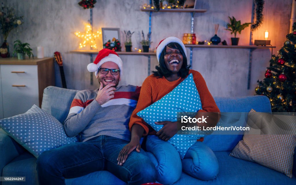 Young couple watching tv at home Young multiracial couple watching a comedy movie in the living room at night during cozy Christmas holidays Christmas Stock Photo