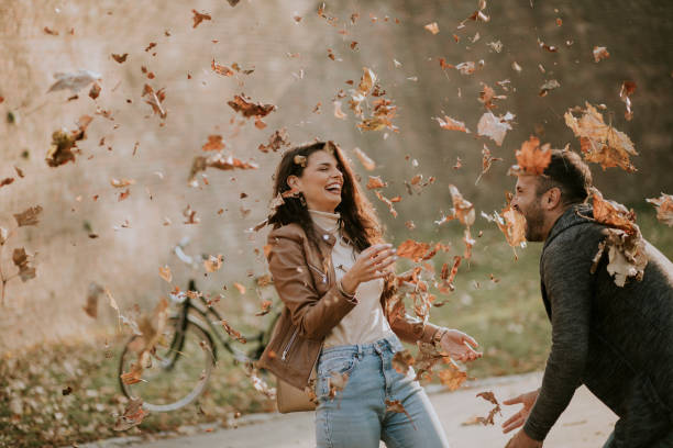 Young couple having fun with autumn leaves in the park stock photo