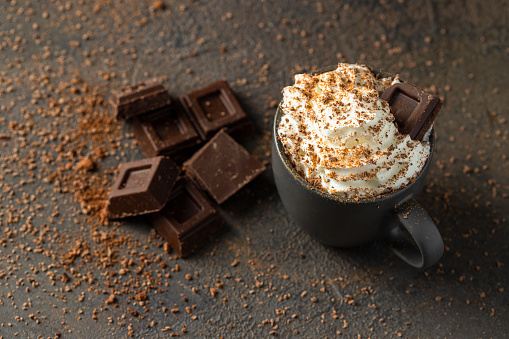 Hot chocolate  cup with whipped cream  and chocolate slices  on dark concrete background. Warm cozy beverage for cold days