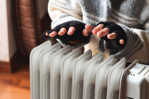 Persona calentando sus manos en casa sobre un radiador portátil doméstico en invierno photo