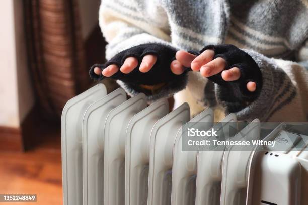 Person Heating Their Hands At Home Over A Domestic Portable Radiator In Winter Stock Photo - Download Image Now