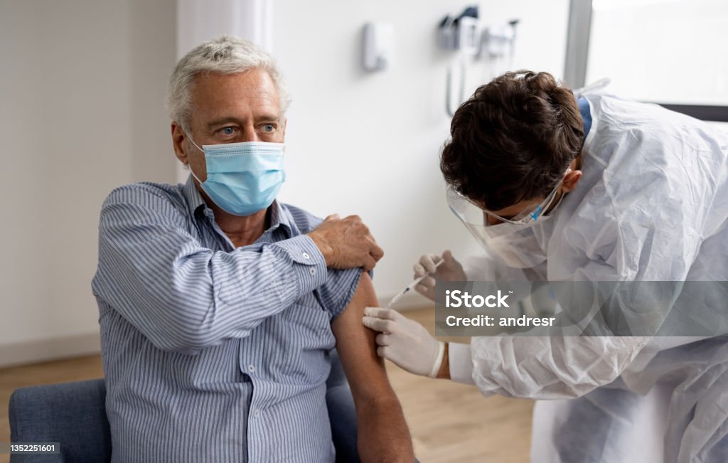 Adult man getting a booster dose of the COVID-19 vaccine at the hospital Latin American adult man getting a booster dose of the COVID-19 vaccine at the hospital - stop the pandemic concepts Vaccination Stock Photo