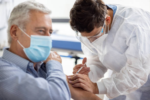 Healthcare worker giving a COVID-19 vaccine to an adult man at the hospital stock photo