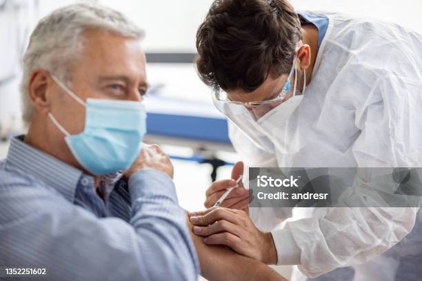 Healthcare Worker Giving A Covid19 Vaccine To An Adult Man At The Hospital Stock Photo - Download Image Now