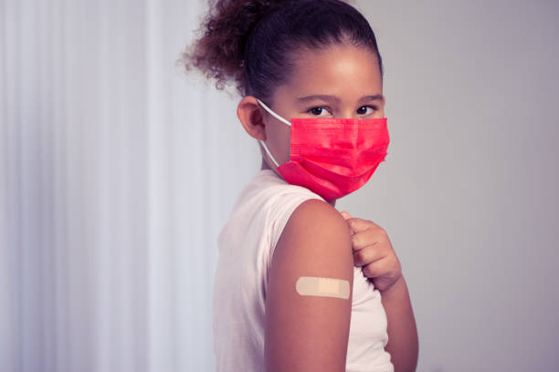 Little girl in mask showing  bandage. Girl showing her arm after getting vaccinated or inoculated due to spread of coronavirus, population, social or herd immunity, vaccine effect concept. herd immunity photos stock pictures, royalty-free photos & images