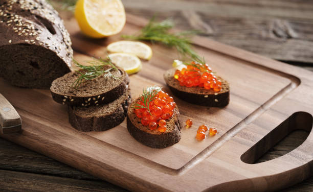 caviar rojo con pan negro, eneldo y limón sobre tabla de madera - plank bread caviar close up fotografías e imágenes de stock