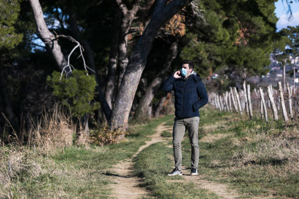 istock Man with surgical mask protecting himself from corona virus talking on mobile 1352262488