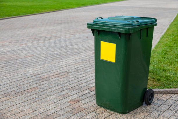 istock Plastic green garbage can for collecting garbage in the park. Mobile trash can with wheels. A yellow sign marks plastic waste 1352262793