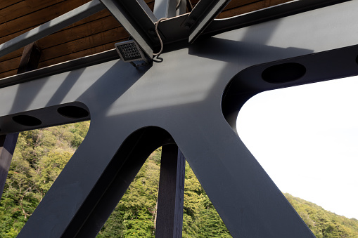 A fragment of a metal structure of a pedestrian crossing over a river or highway. Angular connection of several iron beams in one place. Modern industrial architecture. Close-up.