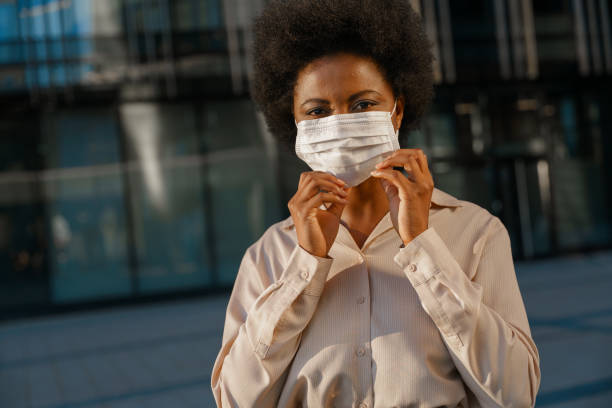 istock A dark skinned girl, adjusting a protective face mask, looking in a camera in a sunrise light on a city square 1352266534