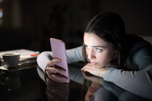 Worried woman checking smart phone in the dark night