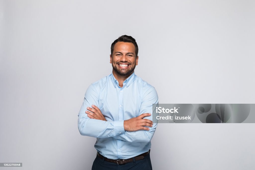 Portrait of cheerful mid adult businessman Portrait of handsome mid adult man wearing blue shirt, standing with arms crossed and smiling at camera. Studio shot of male entrepreneur against grey background. Men Stock Photo