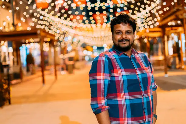 Portrait of a Cheerful Indian Man Standing Under Warm Tungsten-Colored String Lights on Larimer Square in Denver, Colorado at Night