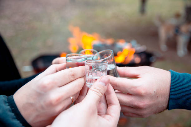 Heating with shots and fire outside in autumn picnic Cropped image of hands toasting with vodka shots. Friends drinking shot alcohol outdoors by the fireplace with fire burning. Shot drink outdoors for warming up. Closeup view serbian raki stock pictures, royalty-free photos & images