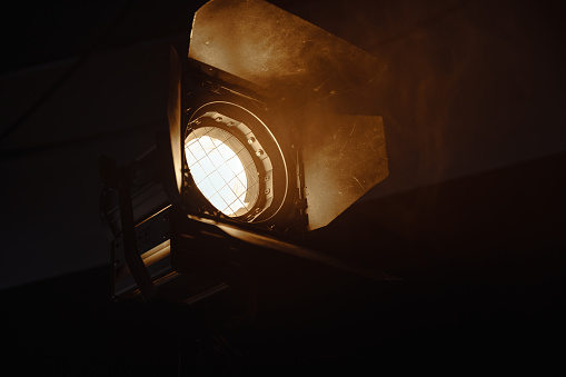 Photo of a professional cinema light with a fresnel lens. A powerful lighting device that is used for professional lighting of scenes in movies and theaters. Close up of a spotlight on the empty stage with copy space