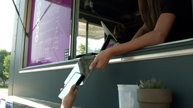 Young Woman's Hand Holding a Smartphone to Scan for NFC Mobile Cashless Payment at a Food Truck Concession Stand