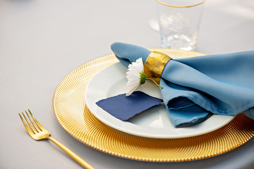 Elegant and chic wedding table setting in gold and blue colors and fresh flowers. Soft selective focus.