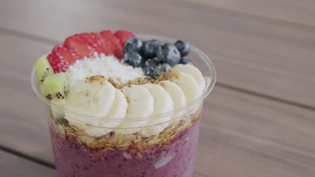 Close-Up Handheld Shot of a Healthy Acai Food Bowl on a Wooden Table Outdoors in the Summer