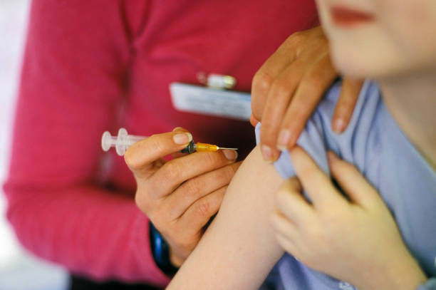 Child receiving their MMR vaccination A child about to be given the MMR (mumps, measles, rubella) vaccination into their arm by a surgery nurse with a hypodermic syringe, England, UK. measles stock pictures, royalty-free photos & images