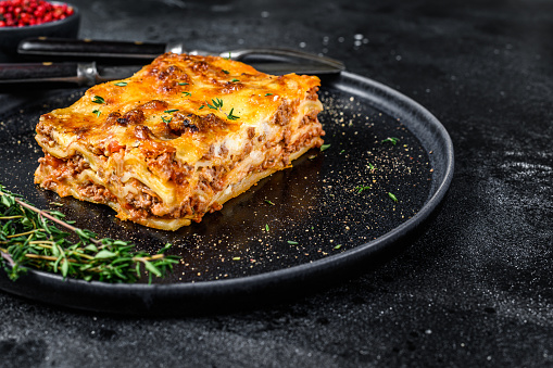 Lasagna with mince beef meat and tomato bolognese sauce on a plate. Black background. Top view. Copy space.