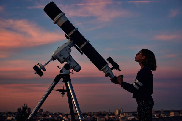 istock Girl with astronomical telescope stargazing under twilight sky. 1352278921