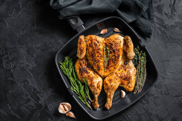 istock BBQ spatchcocked barbecue whole chicken on grill pan. Black background. Top view 1352279717