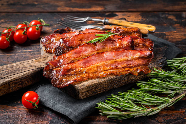 Roasted pork Bacon sizzling slices on wooden board. Wooden background. Top view Roasted pork Bacon sizzling slices on wooden board. Wooden background. Top view. cooked bacon slice stock pictures, royalty-free photos & images
