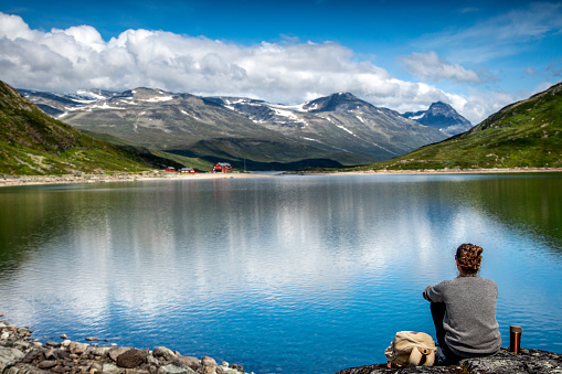 Woman traveler sitting by the lake overlooking the mountains. Travel to Novegia