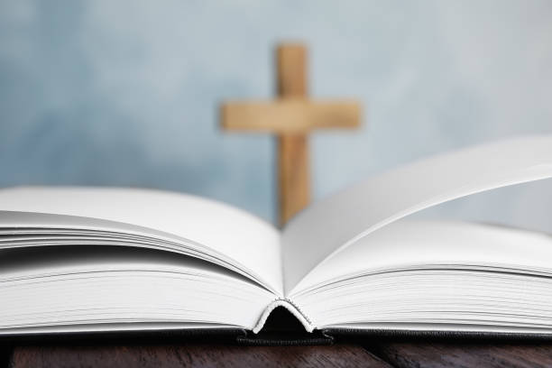 istock Open Bible on table and blurred cross on background, closeup. Christian religion 1352283724