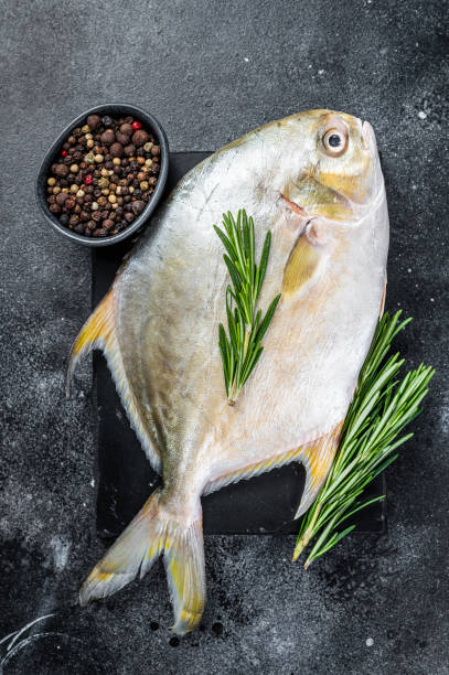 istock Raw fish pompano with herbs on a  marble board. Black background. Top view 1352284165