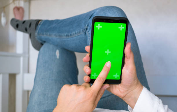 istock Woman at Home Lying on a Couch using Smartphone with Green Mock-up Screen, 1352284329