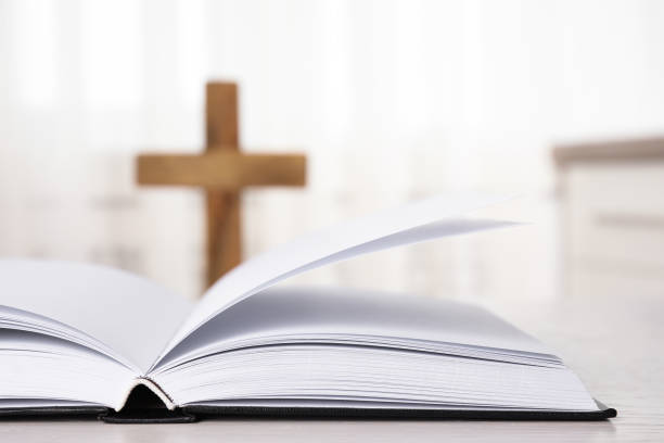 istock Open Bible on table and blurred cross on background, closeup. Christian religion 1352284347
