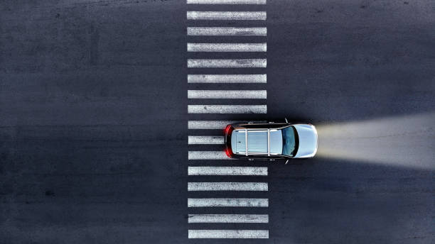 Aerial. A car with its headlights on drives over a pedestrian crosswalk at night. Top view from drone. stock photo