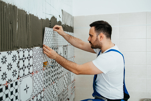 Professional builder applying ceramic tiles on a wall. Home building and decorating concept.