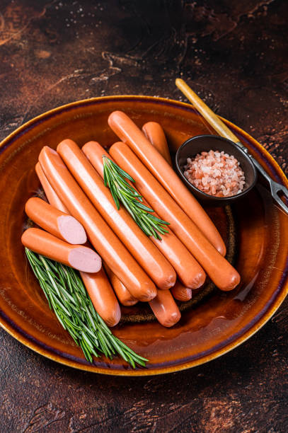 istock Frankfurter raw sausages in a rustic plate with herbs. Dark background. Top view 1352284720