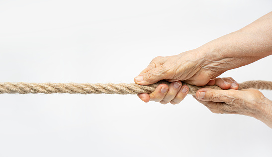Tug of war. Aged wrinkled hands pull the rope towards themselves.