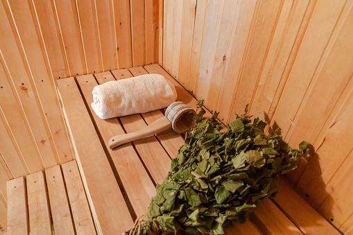 Traditional old Russian bathhouse SPA Concept. Interior details Finnish sauna steam room with traditional sauna accessories set towel birch broom scoop felt. Relax country village bath concept