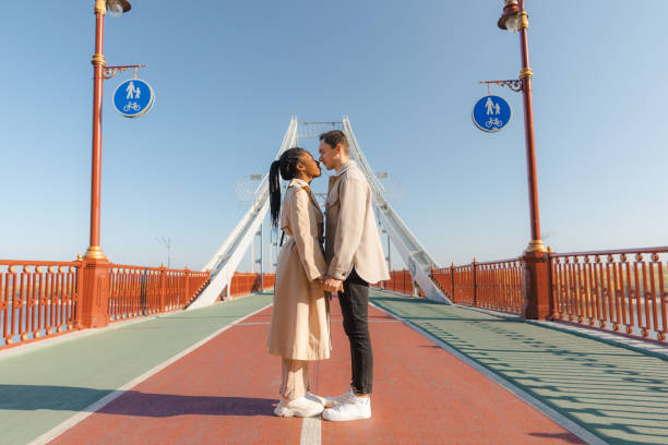 чернокожая женщина и кавказец стоят на мосту и целуются - couple autumn embracing bridge стоковые фото и изображения