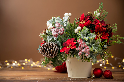 Christmas festive arrangement with red poinsettia on brown background with bokeh lights